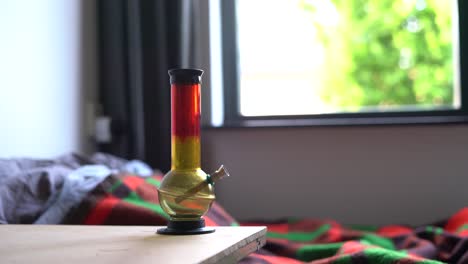 Red-and-yellow-bong-standing-next-to-bed,-drug-addiction,-habit-routine-recreational