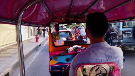 Ein-Tuk-Tuk,-Das-In-Bangkok-Vom-Beifahrersitz-Aus-Gesehen-Auf-Der-Linken-Straßenseite-Fährt,-Während-Die-Leute-Auch-Auf-Dem-Bürgersteig-Zu-Sehen-Sind
