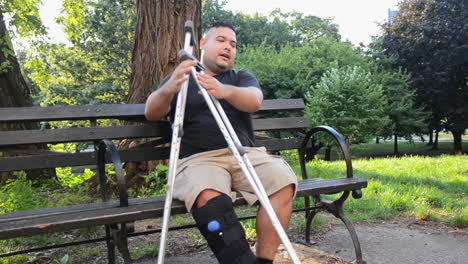 Young-Man-with-a-Medical-Boot-and-Crutches-Sits-on-a-Bench