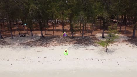 Drone-shot-of-Man-Lying-on-the-green-Air-Sofa-on-the-Sandy-Beach-with-tent-behind