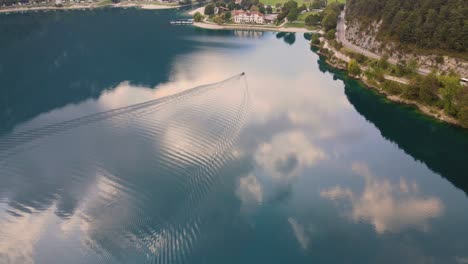 Drone-goes-down-following-a-little-boat-on-Ledro-lake,-Trentino,-Val-di-Ledro-in-North-Italy
