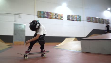 Young-male-kid-jumping-over-ramps-at-indoor-skate-park