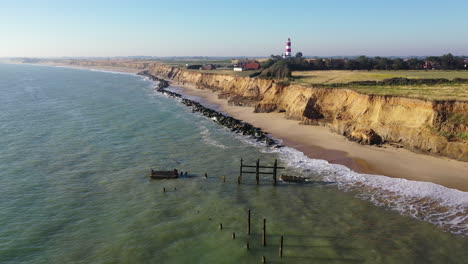 Steady-footage-by-drone-of-the-sea-defences-at-Happiburgh,-Norfolk-Uk-with-the-lighthouse-in-the-background