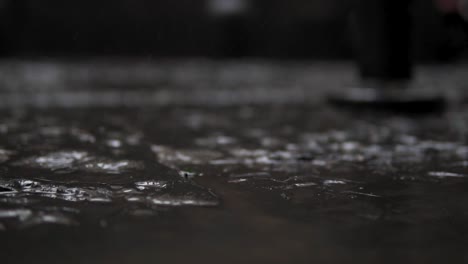 Rain-drops-falling-on-ground-close-up,-droplets-splashing-on-stone-surface