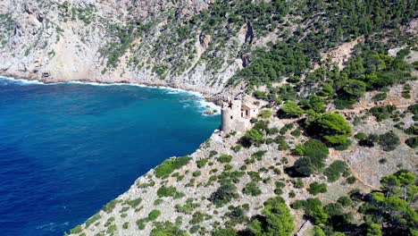 Tower-Of-Basset-Cove-In-Mallorca-Spanien-Mit-Touristen,-Die-Das-Blaue-Wasser-Unten-Erkunden-Und-Bewundern,-Luftwagen-Aus-Der-Luft-Enthüllt
