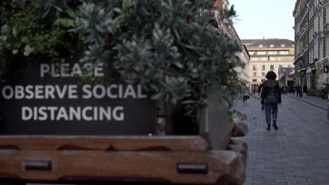 People-walk-past-a-sign-on-a-decorative-handcart-that-says,-“Please-observe-social-distancing”-in-a-very-quiet-Covent-Garden-during-the-second-national-Coronavirus-lockdown