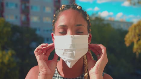 Portrait-of-Serious-Young-Mixed-Race-Woman-With-Hair-Braids-Taking-Off-Face-Mask-in-Exterior-on-Sunny-Summer-Day,-Looking-at-Camera,-Full-Frame