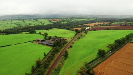 Aerial-still-shot-with-a-steam-train-traveling-towards-camera,-middle-of-English-countryside