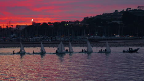 Sailboats-being-towed-through-sea-harbor-to-docks-during-beautiful-colorful-sunset-on-the-ocean