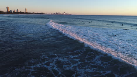 Aerial-of-drone-tracking-surfer-along-breaking-waves-with-Surface-Paradise-QLD-in-the-background-during-sunrise-at-the-popular-tourist-destination-Burleigh-Heads-Gold-Coast-QLD-Australia
