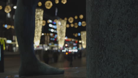 Statue-foot-and-blurred-background-of-street-decorated-with-Christmas-lights