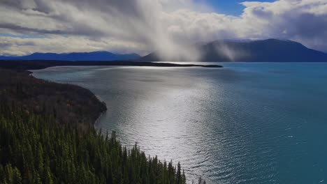 Fly-over-lakeside-Atlin-Lake-with-sun-rays-through-clouds,-Canada