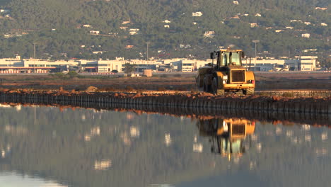Smooth-follow-a-tractor-reflected-in-the-water-of-the-Salinas-de-Ibiza,-Spain