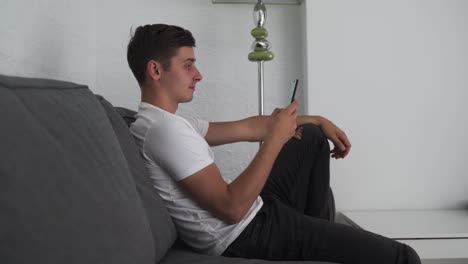 Happy-young-man-uses-a-smartphone-while-sitting-on-a-sofa