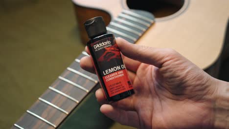 Man-Holding-And-Showing-The-Bottle-Of-Lemon-Oil-Cleaner-And-Conditioner-For-Guitar-Fingerboard-Maintenance