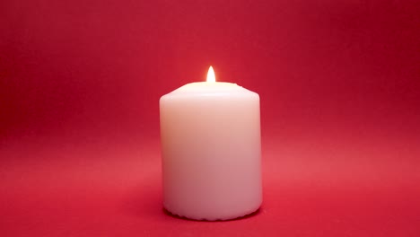 Lighting-white-candle-with-match,-illuminated-red-background-in-studio