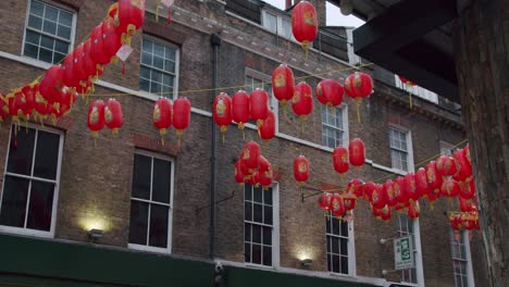 Chinese-lantern-reveal-from-alleyway-in-Chinatown-London,-swaying-in-the-wind-on-an-overcast-day