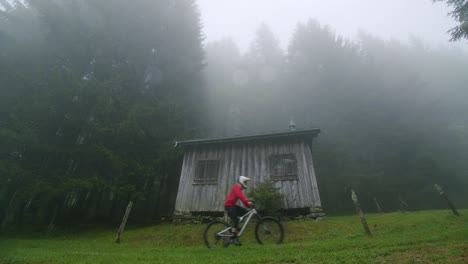 Mountain-biker-rides-past-an-abandoned-cabin-in-a-foggy-forest