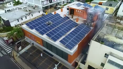 Aerial-view-overlooking-firefighters-on-store-building,-a-structure-with-solar-cells-on-the-roof,-burning-in-San-Diego,-California,-USA,---orbit,-drone-shot