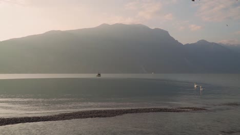 Mystic-light-of-sunrise-on-lone-mountain,-golden-morning,-empty-Lake-Garda-shore