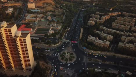 High-Angle-Aerial-Shot-Over-Towers-in-Sunset-Near-the-Square-in-Big-City-Tehran-Iran-Cars-Drive-in-Streets-Taxi-Stop-at-Taxi-Station-and-Cityscape-and-Green-Spaces-in-Background-Landscape