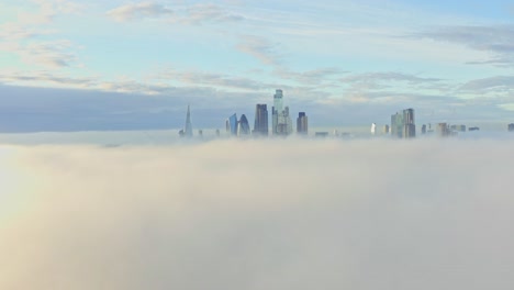Dolly-back-aerial-shot-over-morning-fog-towards-London-city-centre-skyscrapers-sunrise