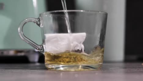 Kochendes-Wasser-Wird-In-Einen-Glasbecher-Gegossen,-Der-Einen-Teebeutel-Enthält