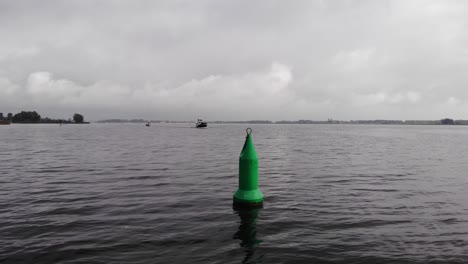 Pasando-Una-Boya-De-Navegación-Mientras-Un-Barco-Navega-En-El-Canal-Marcado-En-Un-Día-Nublado-En-Los-Países-Bajos