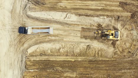 Aerial-top-down-view-of-an-excavator-loading-crushed-stone-into-a-dump-truck-in-a-crushed-stone-quarry