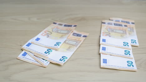 Mano-Masculina-Compartiendo-50-Euros,-Billetes-De-Papel-Moneda,-En-Dos-Montones,-Sobre-Una-Mesa-De-Madera