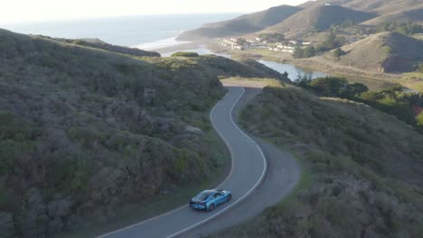 Driving-BMW-i8-sports-coupe-in-Marin-Headlands-scenic-road-at-sunset-aerial-view
