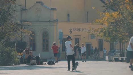 Young-teenager-riding-skateboard-in-European-square,-summertime,-Bratislava,-Slovakia,-day,-full-shot,-handheld