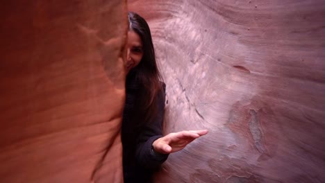 Young-happy-female-hiker-works-her-way-through-a-tight-slot-canyon-in-Southern-Utah,-Slow-motion-following-camera-shot