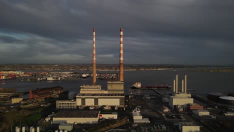 Alte-Schornsteine-Des-Poolbeg-kraftwerks-In-Dublin,-Irland-Unter-Dunklem-Himmel-Mit-Dublin-hafen-Im-Hintergrund---Breite-Luftaufnahme