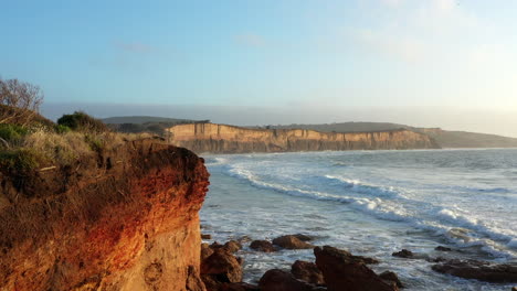 AERIAL-Reveal-Of-Waves-Rolling-Into-Eroded-Cliffs-During-Golden-Hour