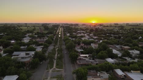 Dolly-in-flying-over-boulevard-main-street-and-Santa-Elisa-countryside-town-houses-at-sunset-with-bright-sun-setting-in-the-horizon,-Entre-Rios,-Argentina