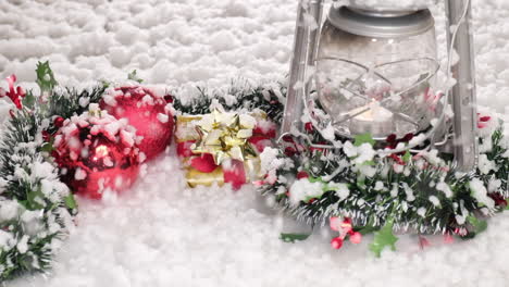 Snow-falling-on-Christmas-decoration-red-and-green-garland,-lamp-and-gif-at-slow-motion