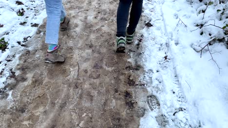 Slow-motion-top-down-of-two-women-with-tramping-boots-walking-on-thawed-snowy-path-outdoors-during-walk-in-nature