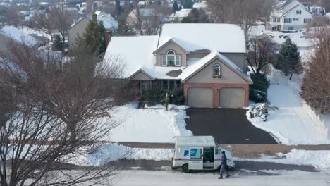 USPS-Mail-Man-drops-Christmas-present-package-at-snow-covered-home-during-Christmas-winter-holiday-season,-aerial-drone-view