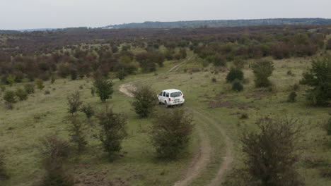 White-jeep-driving-on-a-bumpy-dirt-country-road,bushy-steppe,aerial
