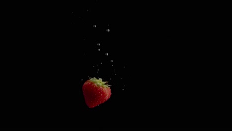 Erdbeere-Fällt-Ins-Wasser-Super-Slowmotion,-Schwarzer-Hintergrund,-Viele-Luftblasen,-4k240fps