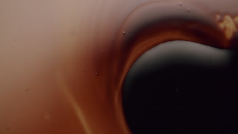 Macro-shot-of-a-black-viscous-liquid-spreading-over-another-amber-liquid