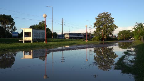 Der-Verkehr-Auf-Einer-Bundesstraße-Spiegelt-Sich-Auf-Einer-überfluteten-Nebenstraße-In-Einer-Kleinstadt-Auf-Dem-Land