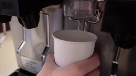 Ice-dispenser-filling-a-white-paper-cup,-in-slow-motion