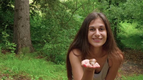 A-woman-on-a-hike-in-a-green-forest-holding-a-snail-and-blowing-it-a-kiss-to-the-camera