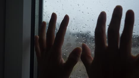 Two-hands-against-a-window-during-a-rainy-day