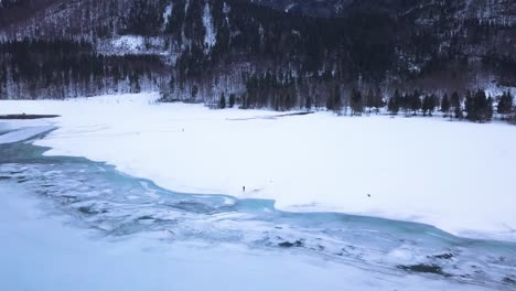 Zwei-Personen-Stehen-In-Einem-Großen-Schneefeld-In-Einem-Tal-Mit-Einem-Eisigen-See