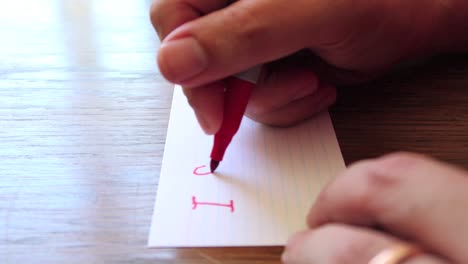 close-up-footage-as-male-hands-write-a-note-using-permanent-marker-pen-on-a-small-card-of-paper