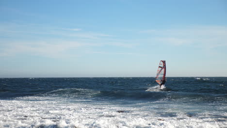 Pan-shot-of-a-norwegian-windsurfer-changing-direction,-while-sailing-on-the-North-sea,-in-the-atlantic-ocean,-on-a-sunny,-summer-day,-in-Lista,-South-Norway