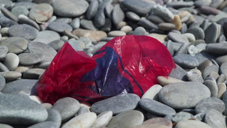 Rote-Plastiktüte,-Die-Einen-Kiesstrand-Verunreinigt,-Langsam-Heranzoomen